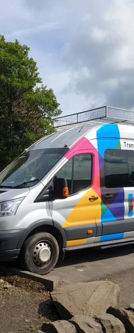 Glasgow Kelvin College branded minibus and trailer parked beside a rock face under a cloudy sky. Glasgow Kelvin College branded minibus and trailer parked beside a rock face under a cloudy sky.